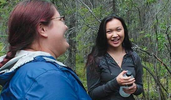 Two Ahtna interns talking and smiling in the woods