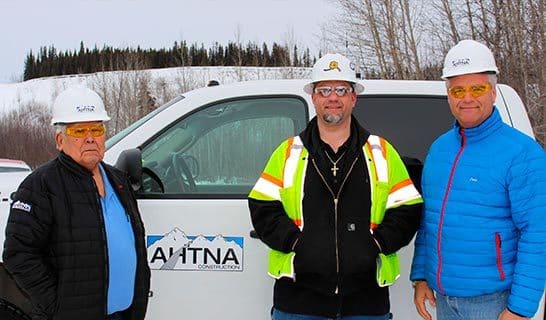Outdoor photo of three Ahtna Engineers in front of Ahtna truck, smiling at camera
