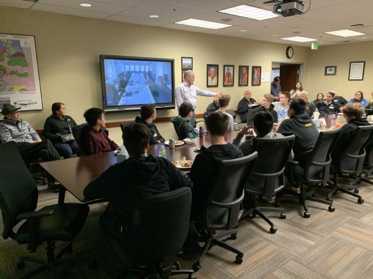 Photo of conference room with Tom Maloney speaking and Glennallen students