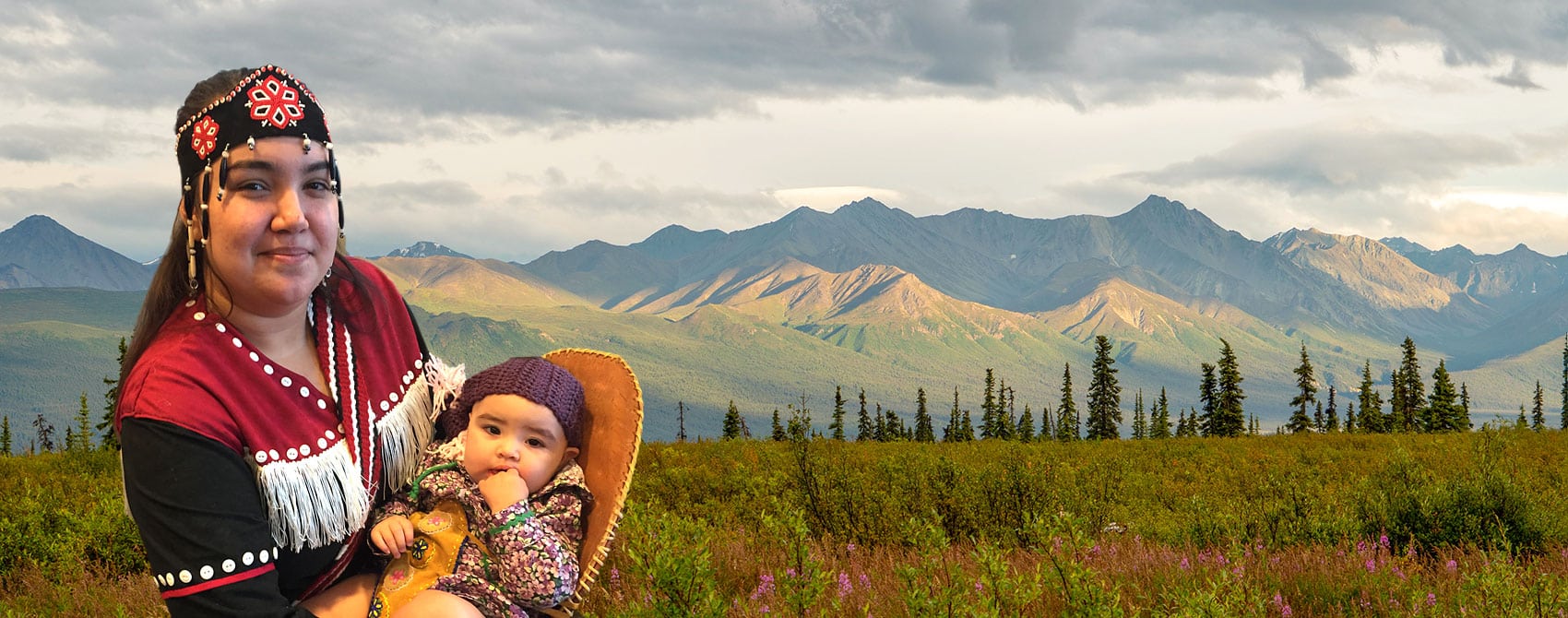 Woman and baby in traditional native dress with Ahtna mountains in the background.