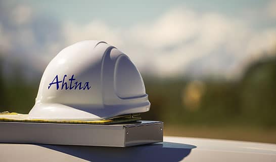 Ahtna hardhat sitting on a manual with Alaskan mountain in the background.