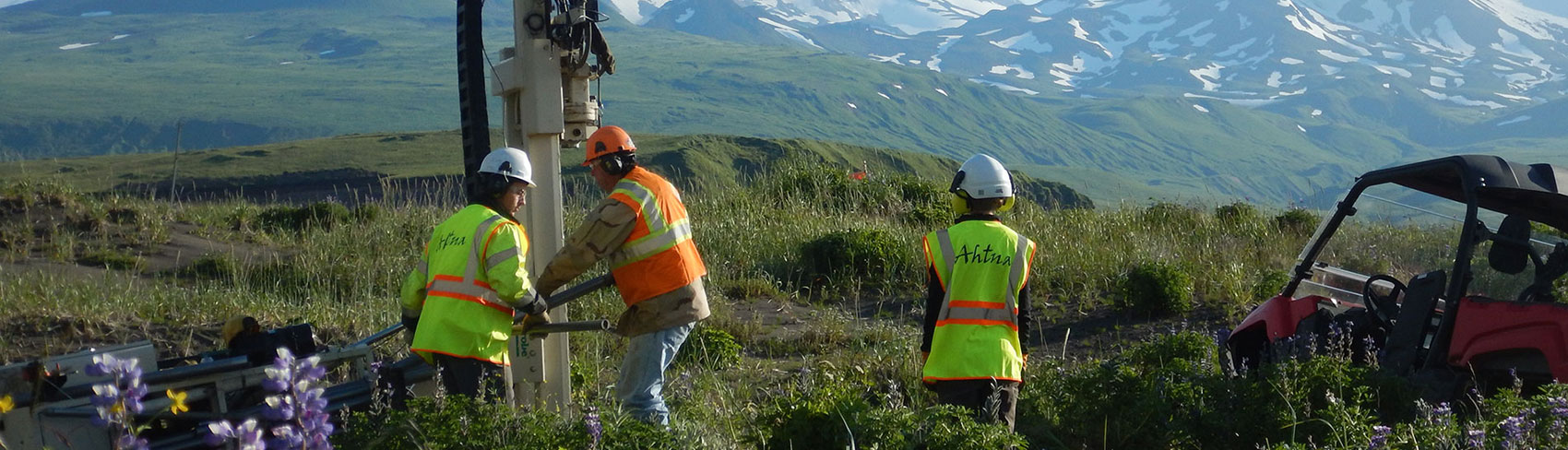 Workers fix a drill in the middle of the Alaska tundra with mountains in the background.