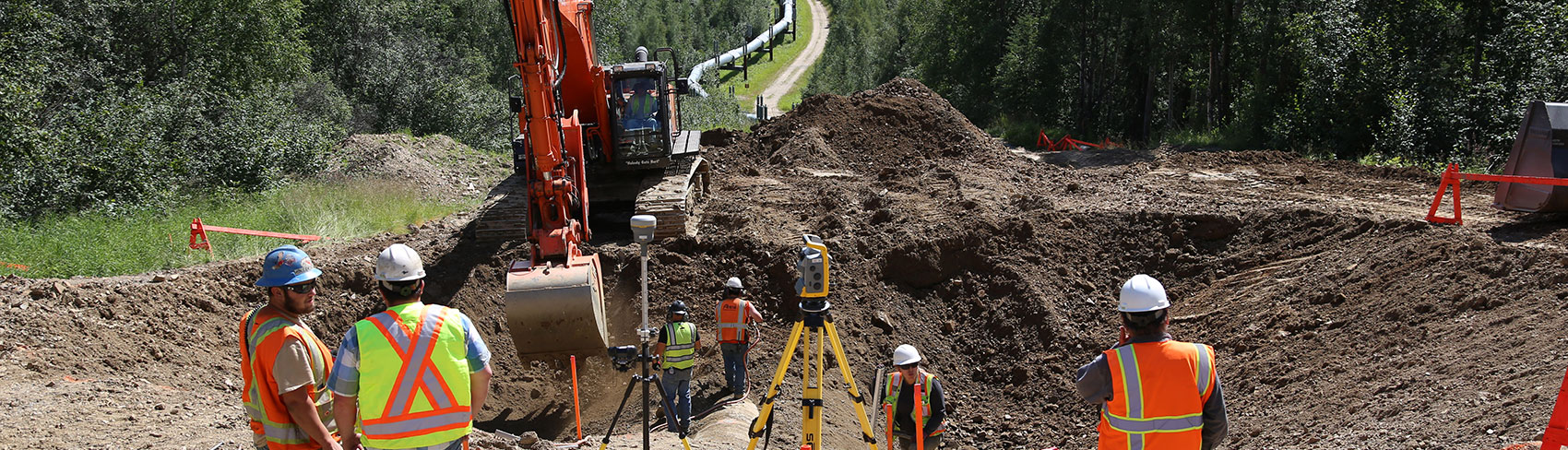 Workers with excavator and Alaska pipeline in the background.