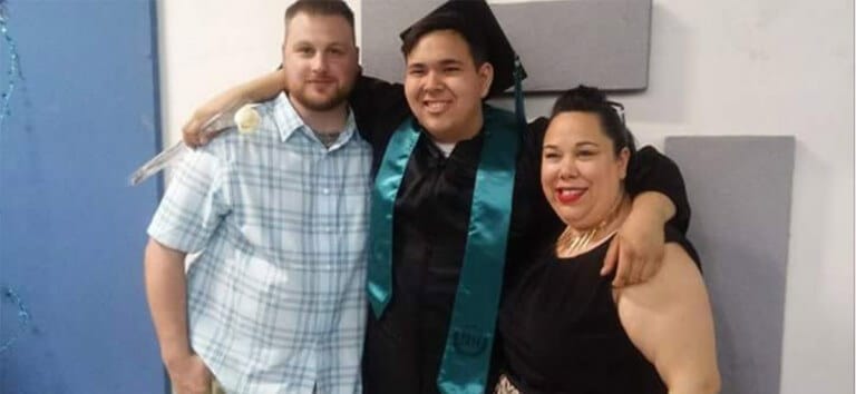 Jason wearing cap and gown with arms around friends smiling at camera